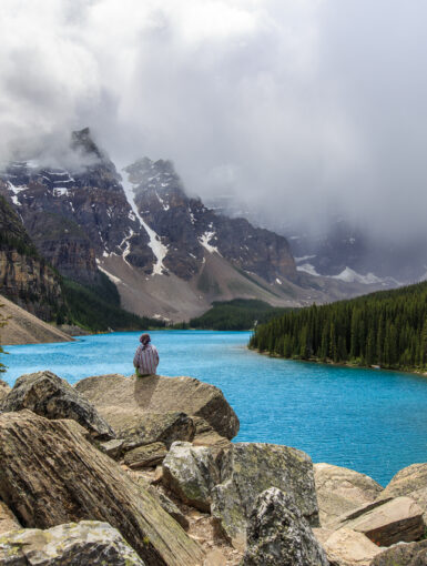 A lone girl sits on a pile of rocks overlooking Moraine Lake in Banff National Park